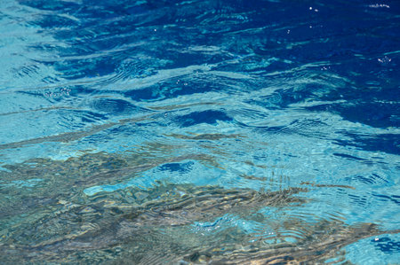 Sunlit ripples and reflections on clear blue pool water, close-up texture background.の写真素材