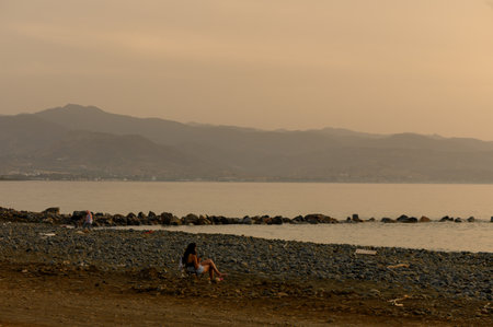 A peaceful scene of a girl sitting alone on the seashore in Cyprusの写真素材