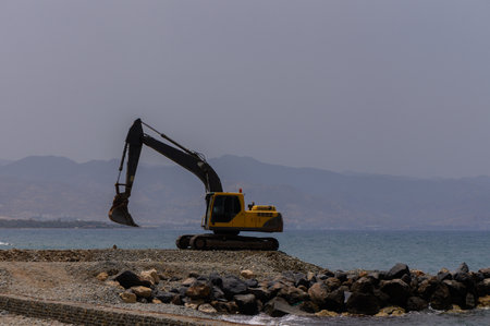 A yellow excavator is working near the coastline of the Mediterranean Sea on a sunny day in Cyprusの写真素材