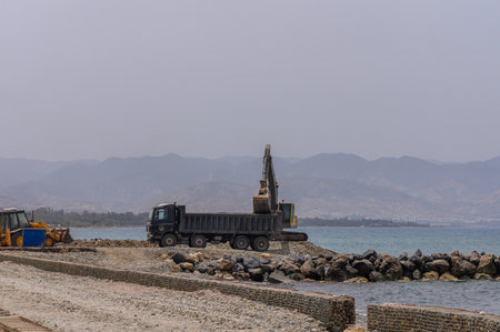 Excavator Loading Sea Rocks into Dump Truck by the Shore in Cyprusの写真素材