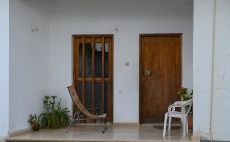 Cozy terrace at the entrance of a traditional Cypriot house featuring a sunbed and white plastic chairs for outdoor relaxation.の写真素材