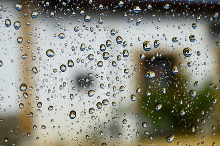 Water droplets on a car window glass after rain, creating a natural abstract texture with soft light and blurred background.の写真素材