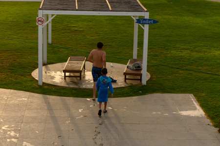 A teenage boy and a younger child walk away from the pool beneath a sunny canopy on a warm day in Cyprus.の写真素材