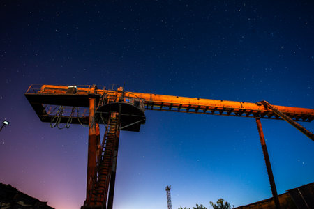 Large gantry crane stands motionless at a scrap metal yard under a sky full of stars, capturing industrial silence at night.の写真素材