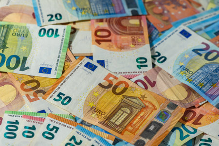 Scattered euro bills of 10, 20, 50, 100, and 200 spread out as textured financial background,...