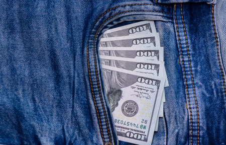 Close-up of 100 US banknotes sticking out of a jeans pocket, symbolizing cash, wealth, savings, finance, and everyday moneyの写真素材