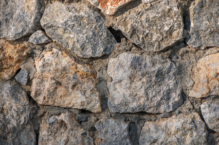 Rough textured stone wall in Cyprus illuminated by warm sunlight, showcasing rustic Mediterranean...