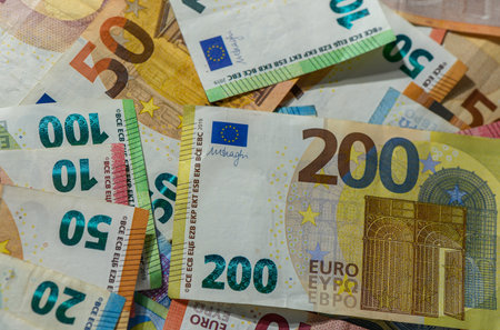 Scattered euro banknotes of 10, 20, 50, 100, and 200 denominations forming a colorful background,...