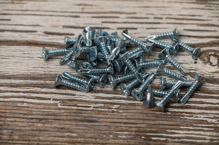 Metal roofing screws scattered on an aged wooden table, ideal for DIY, construction, and hardware...