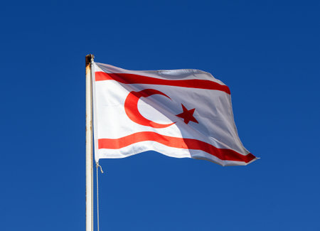 The red and white flag waving on a tall flagpole against a clear blue sky.の写真素材