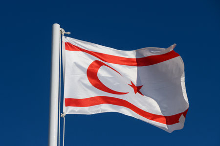 The red and white national flag of Northern Cyprus waving proudly on a tall pole against a clear blue sky.の写真素材