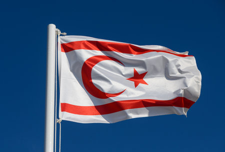 The national flag of Northern Cyprus on a pole, waving in the wind against a blue sky.の写真素材