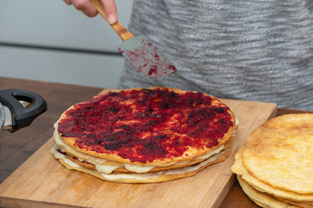 Close-up of a woman evenly spreading berry jam on sponge cake layers using a spatula, dessert preparation.の写真素材