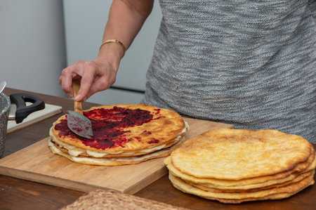 Close-up of a woman evenly spreading jam on sponge cake layers, homemade dessert preparation.の写真素材