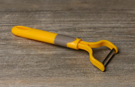 Y-shaped vegetable peeler with sharp blade on old wooden table. Wood relief and metal shine form a practical background for recipes and culinary photosの写真素材