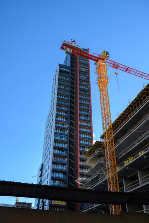 Tall yellow tower crane rises above construction with concrete blocks and materials. Bright color...