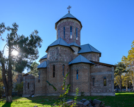 Ancient darkened stone church with wrought cross on dome stands on narrow lane with balconies. Warm...