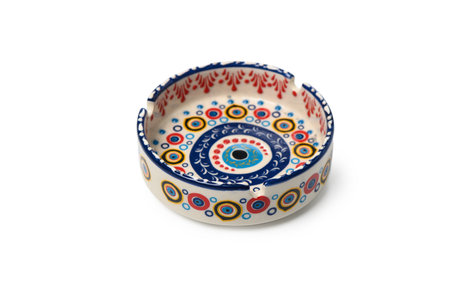 Ceramic ashtray decorated with a traditional Turkish evil eye (Nazar) pattern. Oriental style, handmade decor symbolizing protection from evil. Object isolated on a white background, top view.の写真素材