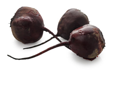 Three cooked beetroots with deep purple hue, professionally arranged on clean white background....