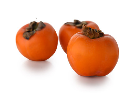 Three luscious persimmons with vibrant orange hue and smooth texture, professionally isolated on clean white background. Ideal for healthy eating and seasonal food photography.の写真素材