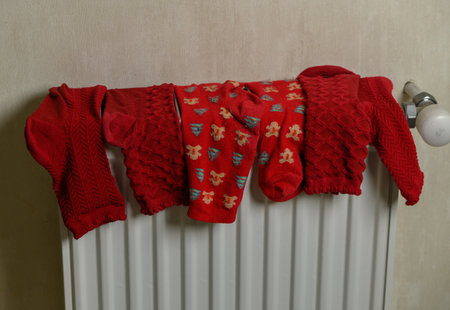 Festive red socks with Christmas patterns hanging on a heater to dry. The cozy winter scene combines holiday cheer with everyday domestic life in a warm, seasonal composition.の写真素材