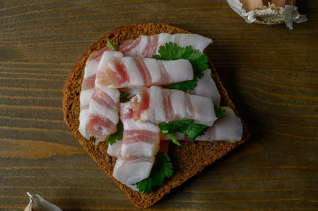 A rustic serving of dark rye bread layered with slices of traditional cured meat, resting on a worn wooden surface. Highlights the rich textures, hearty simplicity, and culinary heritage.