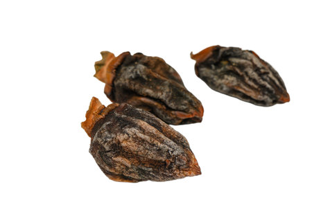 Three naturally dried persimmons with a deep amber hue and softly wrinkled texture, placed on a...