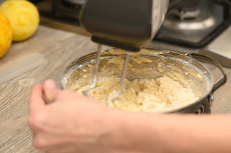 A woman attentively prepares Stollen dough using a hand mixer, surrounded by baking ingredients in a...
