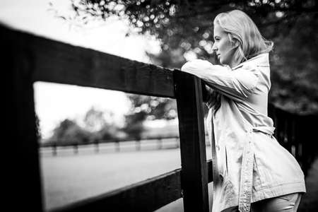 Thoughtful Woman Leaning Up Against Fence In Park, Black And Whiteの写真素材