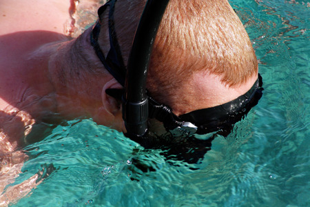 a man in a black snorkeling mask looks under the waterの写真素材