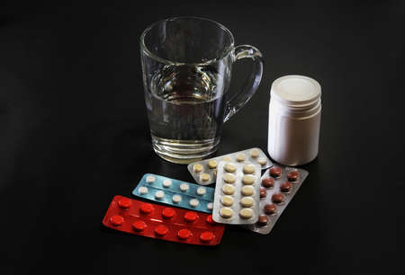 Pills and glass of water on black background. Healthcare, treatment and pharmacy concept