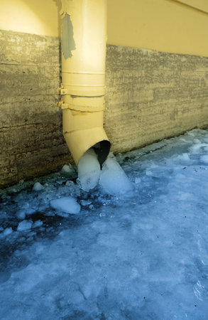 The bottom of a yellow drainpipe with iceの写真素材