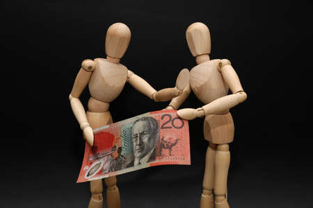 A pair of wooden mannequins talking discussing fighting arguing over financial strain pressure hardship. Struggling over a twenty dollar note. Domestic stress personal money finances debt concept.の写真素材