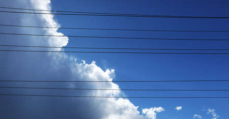 Interesting alternative creative view looking up through power lines to white fluffy clouds building...