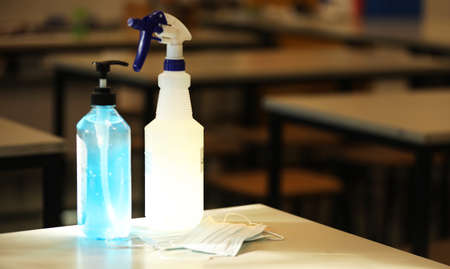 An empty school classroom with desks in the background. A face mask, bottle of hand sanitizer and...