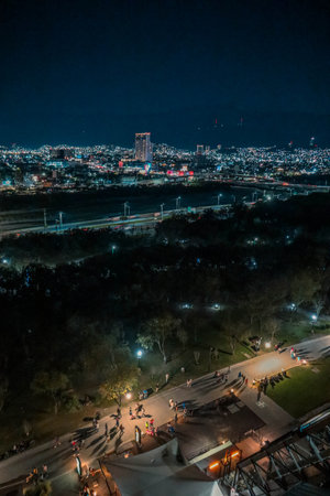 View of a city at night featuring a park with illuminated walkways, distant modern buildings, and vibrant lights across the urban skylineの写真素材