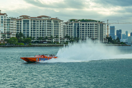 A vibrant orange speedboat speeds across the turquoise waters near South Beach, Miami, as a backdrop of modern city buildings lines the distant horizonの写真素材