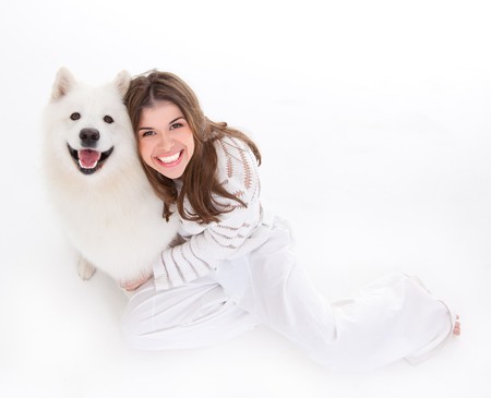 a studio image of a young woman, dressed in white, with her white dog, huging it, both posing, looking up, being happy and smiling.の写真素材