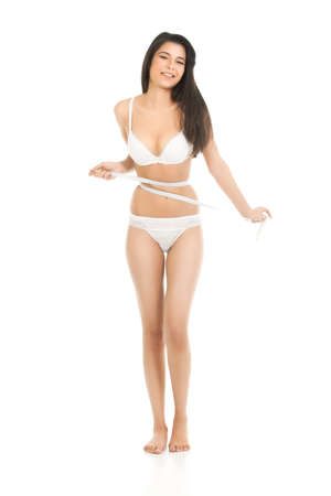 a studio shot of a young, beautiful woman, measuring her waist line. she is dressed in her underwear and she tries to get a smaller number from the measuring meter.の写真素材