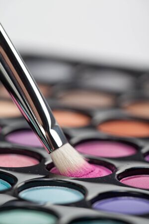 a close-up image of a eye-shadow kit, with a professional makeup brush picking up some pink colourの写真素材