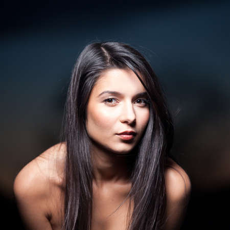 a portrait of a young, beautiful woman, shot outside, on a sunset background. she has a white top on, she looks into the camera, while she leans forwards smiling.の写真素材