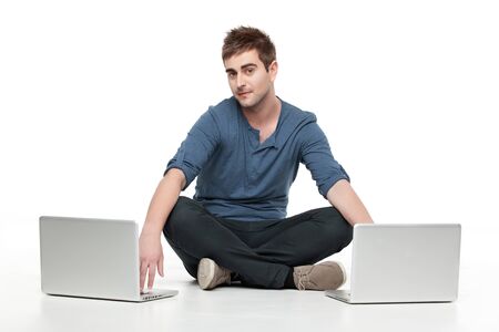 handsome man sitting behind two laptopsの写真素材