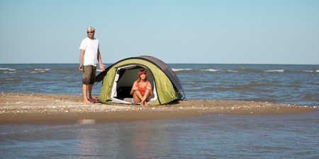 happy young couple sitting on a beach next to their tent, smiling and having a good timeの写真素材