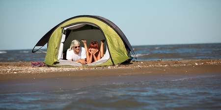happy young sitting in a tent by the sea, talking, enjoying the summer vacationの写真素材