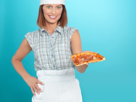 portrait of beautiful young woman chef, holding a pizza slice in one of her hands, on blue backgroundの写真素材