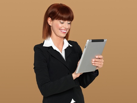 portrait of a beautiful, young businesswoman, working on an electronic computer pad, smiling, on beige backgroundの写真素材