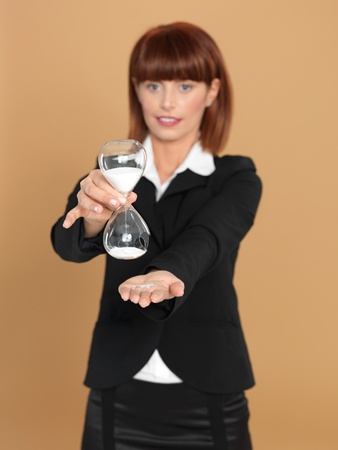 portrait of a beautiful, young businesswoman, holding a broken hourglass in her hands, on beige backgroundの写真素材