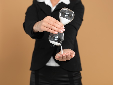 portrait of a beautiful, young businesswoman, holding a broken hourglass in her hands, on beige...
