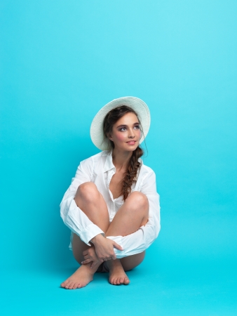 studio fashion portrait of happy, young woman, sitting on blue backgroundの写真素材