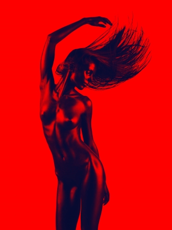 artistic nude of a young woman with black painted skin and red background, in a dance movement, with her hand up in the airの写真素材